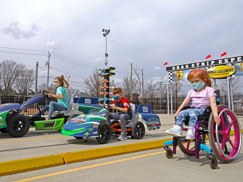 Child in a wheelchair racing against two pedal car racers.